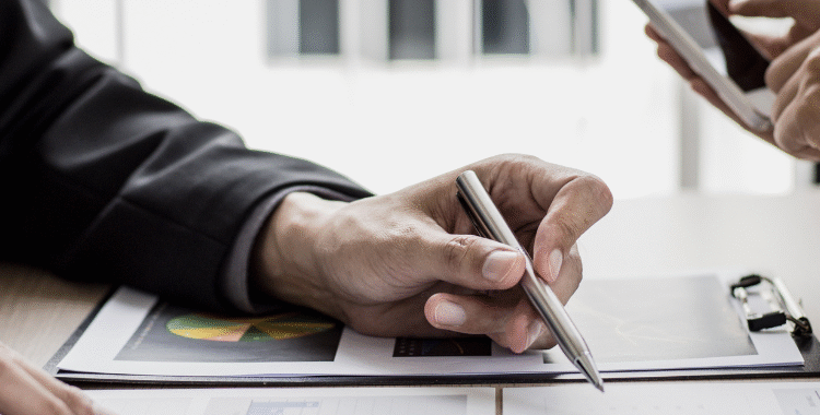 "Hands reviewing financial documents with pen and smartphone, illustrating virtual CFO services for established businesses."